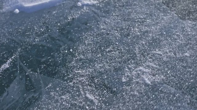 Snow is flying over surface of ice. Snowflakes fly on ice of Lake Baikal. Ice is very beautiful with unusual unique cracks. Snow sparkles and glows in red. Shooting slow motion 180fps. Picture at