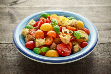 Panzanella Tomato salad with red, yellow, orange cherry tomatoes, capers, basil and ciabatta croutons. summer healthy food.