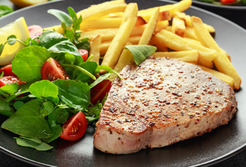 Fried Tuna Steaks on Black Plate with Fresh Green, Tomato Salad, lemon and french fries. healthy sea food