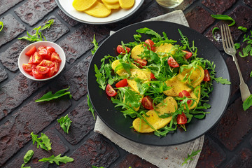 Polenta salad with sea salt, tomatoes, green rocket in a black plate.
