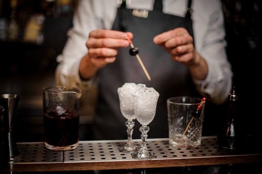 Barman decorating two cocktail glasses with cherries