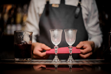 Bartender with two elegant cooled glasses arranged on the bar counter