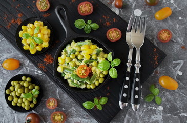 Scrambled eggs with green beans, corn, green peas and fresh Basil in portion a cast iron skillet