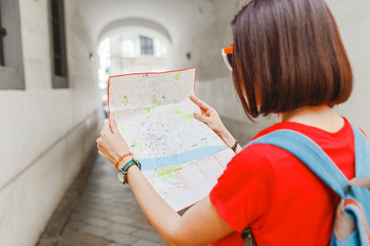 A young happy girl traveler looks at the map and tries to find the right direction for the next attraction in the European city