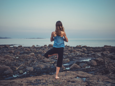 Woman in yoga pose on the coast at sunset