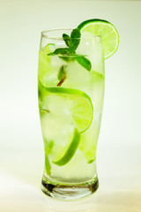 summer cold drink mojito lime and mint with ice and soda with drops on a glass on a white background