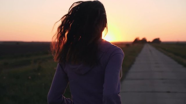 Silhouette of a girl running along the road in the countryside at sunset. Slow motion middle shot