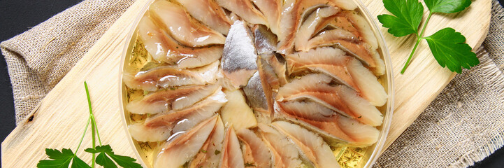 Marinated herring in oil on a wooden board on a gray dark table. Snack. Top view. Copy space.