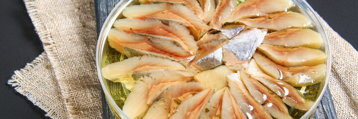 Marinated herring in oil on a wooden board on a gray dark table. Snack. Top view. Copy space.