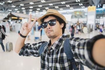 Asian man tourist taking a selfie with smart phone camera in airport.