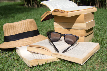 Open books, hat and sunglasses outside on the grass
