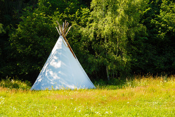 white teepee indian tent standing in beautiful summer landscape.