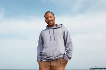 Summer active sports concept. Smiling happy young African-American man hipster in sport hoody on the beach