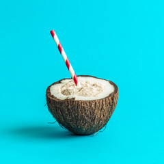 Coconut with drinking straw isolated on turquoise background.