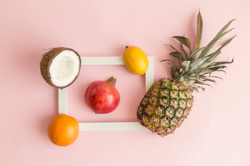 Exotic fruits around photo frame on rose background abstract.