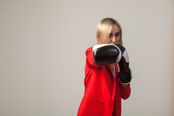 Young beautiful white blond girl in a bright red strict suit with a jacket and white blouse standing in a pose with boxing gloves on a white isolated background