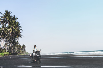 Young woman driving a scooter at the beach with black sand. Bali island.