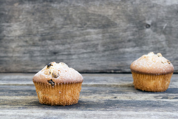 Two muffins with raisins sprinkled with powdered sugar on a wooden background