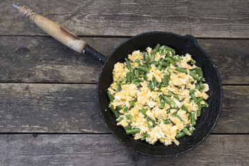 Green beans fried with eggs beautiful in an old frying pan on a wooden background, rustic style