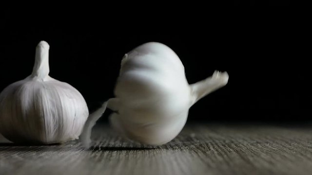 Garlic falling on wooden table against black background 