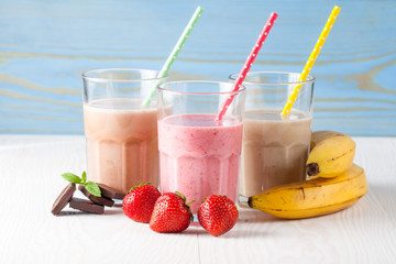 Glasses of milkshakes with chocolate, strawberry, banana flavor, with ice cream on wooden blue and white background. Sweet drinks for summer concept. Shakes and smoothies. Milk shake and cocktail.
