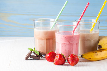 Glasses of milkshakes with chocolate, strawberry, banana flavor, with ice cream on wooden blue and white background. Sweet drinks for summer concept. Shakes and smoothies. Milk shake and cocktail.