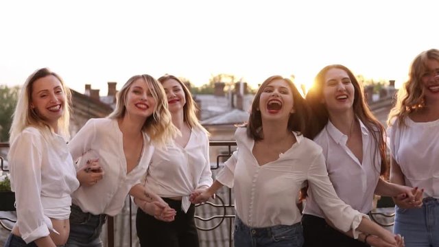 Happy smiling outside on a balcony terrace. Building, city landscape background jumping together in slow motion. Having fun together, fashionable female in same clothes laughing. Enjoyment life