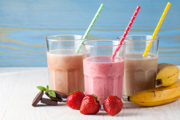 Glasses of milkshakes with chocolate, strawberry, banana flavor, with ice cream on wooden blue and white background. Sweet drinks for summer concept. Shakes and smoothies. Milk shake and cocktail.