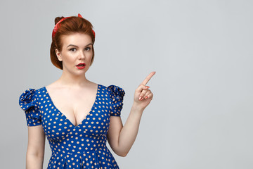 Studio shot of good looking pin up girl wearing vintage outfit staring at camera with jaw dropped,...