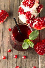 A glass of pomegranate juice with fresh pomegranate fruits on wooden table. Vitamins and minerals. Healthy drink concept.