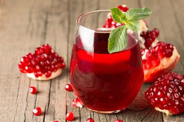 A glass of pomegranate juice with fresh pomegranate fruits on wooden table. Vitamins and minerals. Healthy drink concept.