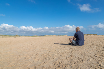 Fototapeta na wymiar Im Sand sitzender Mann mit einem Blick in die Ferne