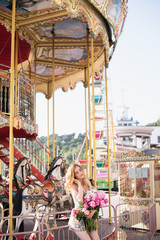 Beautiful girl in a dress with a bouquet of pink peonies in the hands near a vintage carousel