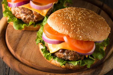 Close-up photo of home made hamburger with beer made of beef, onion, tomato, lettuce, cheese and spices. Fresh burger closeup on wooden rustic table with potato fries and chips.