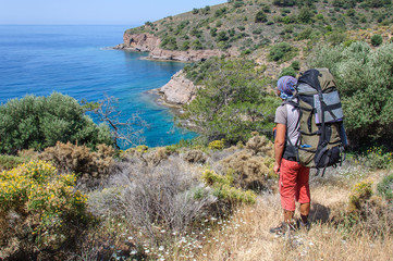 man with a backpack stands on the shore of the Mediterranean Sea and looks into the distance