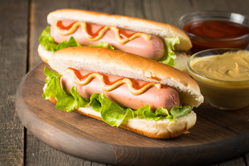Tasty barbecue grilled hot dog with salad,yellow mustard, onion, ketchup, and French fries on wooden background. Junk and fast food concept.