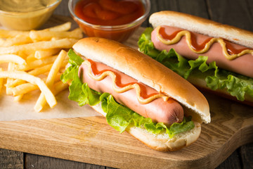 Tasty barbecue grilled hot dog with salad,yellow mustard, onion, ketchup, and French fries on wooden background. Junk and fast food concept.