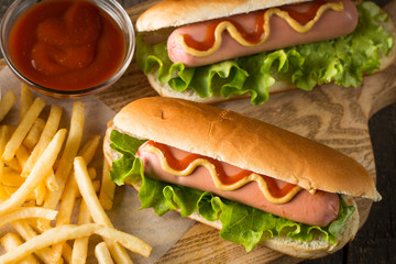Tasty barbecue grilled hot dog with salad,yellow mustard, onion, ketchup, and French fries on wooden background. Junk and fast food concept.