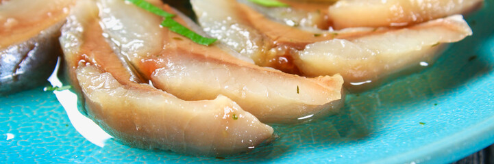Marinated herring in oil on a wooden board on a gray dark table. Snack. Top view. Copy space.
