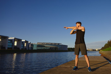 People, sports, fitness and healthy lifestyle concept. Full length shot of athletic active young Caucasian sportswoman warming arms before workout, standing on concrete by river in the morning