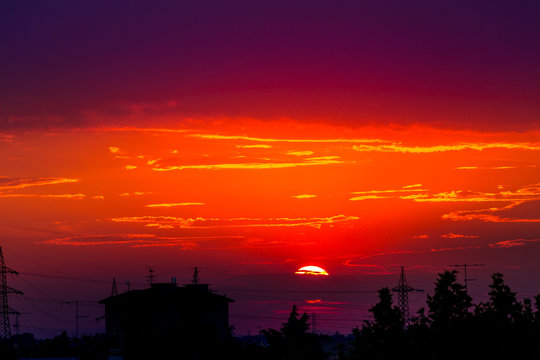Fire red urban sunset with black silhouette of light poles and houses of cityscape. Copy space. Red sunset background.