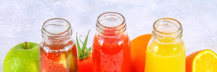 Bottles with fresh orange, apple, tomato juice on a gray concrete table. Fruits and vegetables around.