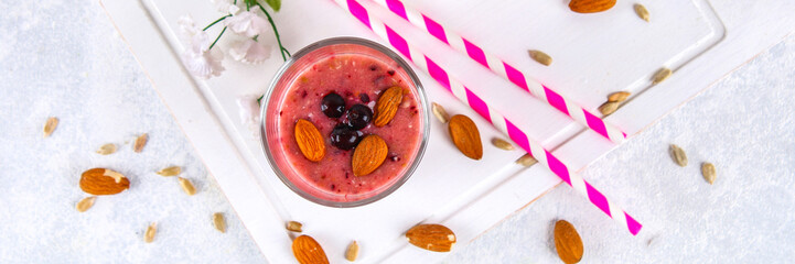 Blueberry smoothies of berries, banana and almonds in glasses with cocktail tubes on a white wooden board.