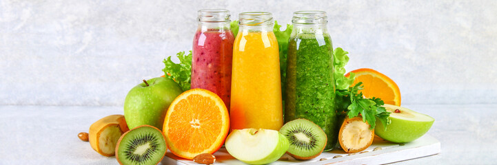 Green, yellow, purple smoothies in currant bottles, parsley, apple, kiwi, orange on a gray table.