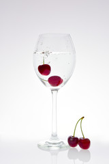 Cherries fall into a glass with sparkling water