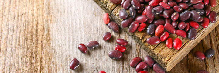 Red raw beans with greens on a wooden table.