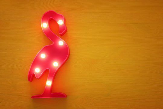 a plastic flamingo lamp with leds over yellow wooden background. holiday summer concept.