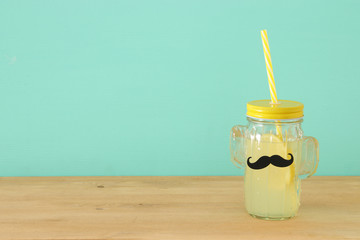 Image of fresh lemonade drink in cute cactus shape glasses wearing mustache, over wooden table. Father's day concept.