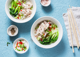 Asian style soup. Rice noodles, boiled chicken, vegetables and broth - delicious diet lunch on blue background, top view. Flat lay