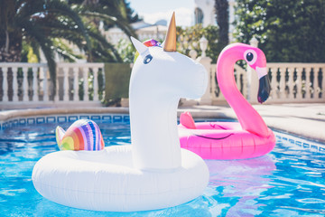 Inflatable colorful white unicorn and pink flamingo at the swim pool. Vacation time in the swimming pool with plastic toys. Relaxation and fun concept